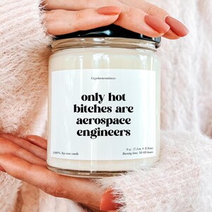 May include: A clear glass jar candle with a black lid. The label reads "only hot bitches are aerospace engineers" in a bold, black font. The candle is 9 oz (7.1cm x 8.9cm) and made of 100% soy wax.