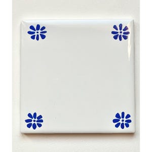 May include: White ceramic tile with four blue floral designs on the corners.