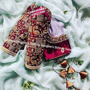 May include: A deep maroon blouse featuring intricate gold embroidery in a grid pattern with peacock motifs. The garment includes long sleeves and a matching set of decorative hanging tassels with gold accents. Text reads STRIMAY DESIGNER'S +919922220369.