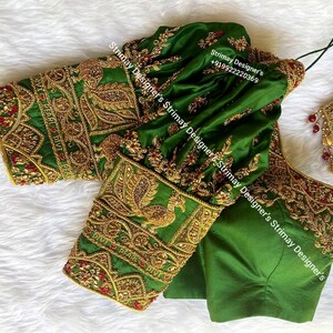 May include: Emerald green blouse with intricate gold embroidery. The sleeves feature a peacock design and floral patterns. Red accents are incorporated throughout the design. The text "Strimay Designer's" is visible on the blouse.