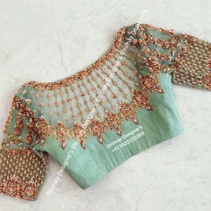 Puede incluir: Una blusa verde menta con intrincados bordados y abalorios. El escote y las mangas transparentes están adornados con delicados diseños. El corpiño presenta detallados diseños florales en tonos dorados y rojos. Las mangas son cortas y están adornadas con abalorios similares.