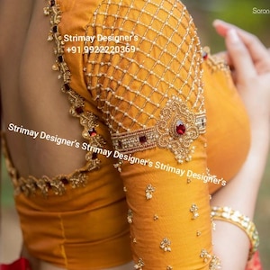 Op de afbeelding: Een mosterdgele blouse met ingewikkeld goudborduurwerk, een ruitpatroon op de mouwen met kleine witte kralen en rode steenaccenten. De tekst Strimay Designer's +91 9922220369 is zichtbaar op de stof, samen met de herhalende merknaam.