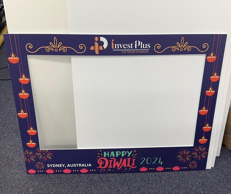 May include: A blue and white photo booth frame with a cutout for a person's head. The frame is decorated with red and orange diya lights and fireworks. The text "Happy Diwali 2024" is printed on the bottom of the frame. The text "Sydney, Australia" is printed on the bottom left corner of the frame. The text "Invest Plus For Smart Investors" is printed on the top of the frame.