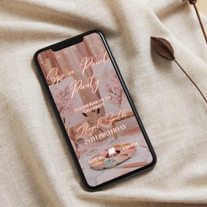 May include: A smartphone displays a digital invitation for a "Sip n' Paint Party" with the text "Please join us to celebrate Angel Smith 25th Birthday" on a pink and white background. The phone rests on a beige fabric.