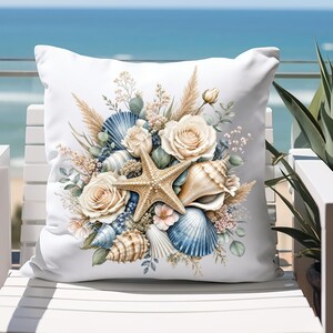 May include: White square throw pillow featuring a coastal design. The pillow showcases a starfish, seashells, and cream-colored roses, with accents of blue and beige. The pillow is placed on a white chair with a view of the ocean in the background.
