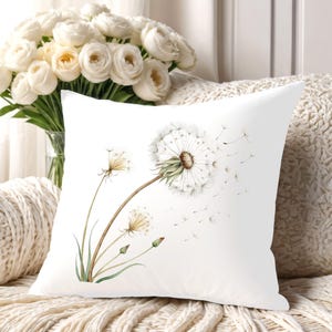 May include: A square white throw pillow featuring a watercolor illustration of dandelion seed heads. The design depicts a large, mature dandelion with seeds blowing in the wind, alongside smaller buds and stems in shades of green and brown.