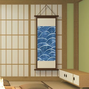 以下が含まれることがあります： 青と白の波模様の日本の掛け軸が壁に掛けられています。掛け軸は濃い茶色の木で額装され、茶色の紐で吊り下げられています。部屋には畳の床、低い木製のキャビネット、障子スクリーンがあります。