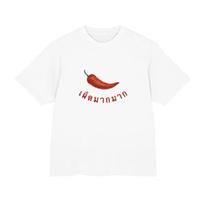 Op de afbeelding: Een wit T-shirt met korte mouwen en een afbeelding van een enkele rode chilipeper in het midden op de borst. Onder de chilipeper staat rode tekst in het Thais geschreven die "เผ็ดมากมาก" luidt. Het T-shirt heeft een ronde hals en een standaard pasvorm.