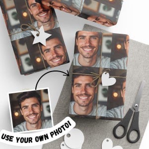 May include: Custom wrapping paper featuring a repeating photographic print of a smiling person wearing a grey shirt. The paper is tied with brown twine and decorated with a white star-shaped tag. A pair of black scissors is placed nearby.