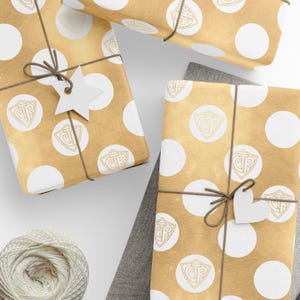 May include: Several wrapped gifts with gold polka dot paper and brown twine. Each package has a white tag and a logo. A ball of twine and a gray cloth are in the lower left corner. The gifts are arranged on a white surface.