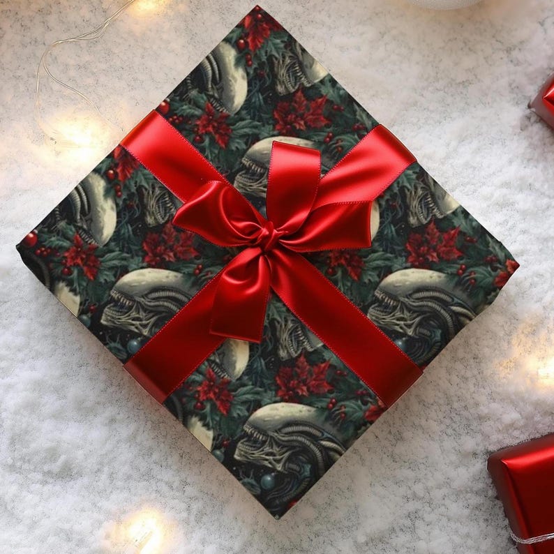A square gift box wrapped in dark patterned paper featuring Xenomorph alien skulls and red poinsettia flowers, tied with a wide shiny red ribbon bow.