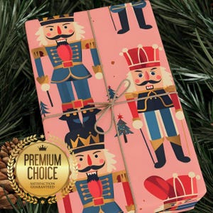 Op de afbeelding: Roze cadeaupapier met een herhaald patroon van speelgoed notenkrakersoldaten in blauwe, rode en gouden uniformen. Het verpakte cadeau is vastgebonden met touw en geplaatst tegen een achtergrond van groene dennennaalden. Een gouden zegel luidt "Premium Choice, Satisfaction Guaranteed."
