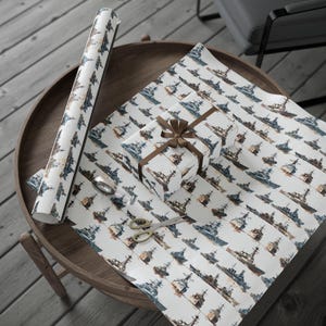 A round wooden table holding an unwrapped roll of warship wrapping paper, a gift box tied with a brown bow, scissors, and tape.