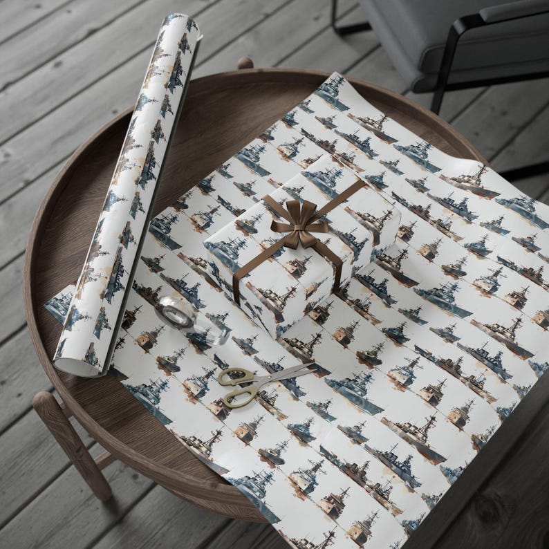 A round wooden table holding an unwrapped roll of warship wrapping paper, a gift box tied with a brown bow, scissors, and tape.