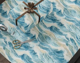 May include: A wrapped gift box with a brown ribbon and bow sits on wrapping paper. The paper and box feature a watercolor design of ocean waves in shades of blue, white, and tan. Scissors and tape are also visible.
