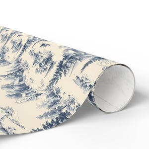 A single roll of wrapping paper printed with a blue and white winter village pattern rests on a white background.