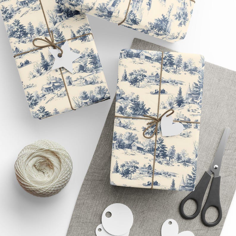 Wrapped gifts, twine, white tags, scissors, and a spool of white string are arranged flat on a gray surface next to blue and white winter village wrapping paper.