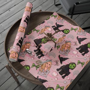 May include: Pink wrapping paper with a repeating pattern of cartoon characters, witch hats, and bows. A wrapped gift with a brown ribbon and a roll of matching paper are on a wooden table. Scissors and tape are also visible.