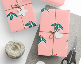 May include: Pink gift boxes wrapped in holly-patterned paper, tied with twine, and adorned with white star and heart-shaped tags. A ball of twine, scissors, and blank tags are also visible, suggesting a holiday theme.