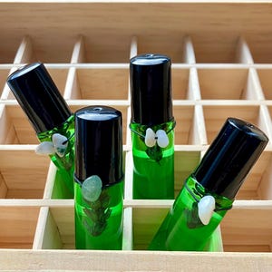May include: Four green glass roller bottles with black caps and white and green accents. The bottles are arranged in a wooden box.
