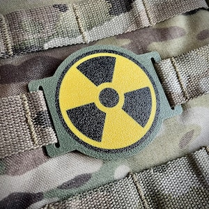 Könnte beinhalten: Ein gelber und schwarzer Strahlungssymbol-Patch, der an einem grünen Molle-Panel befestigt ist.