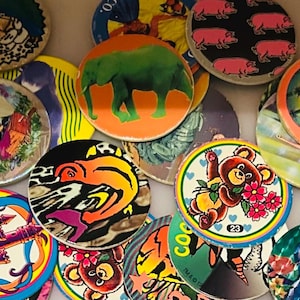 Peut inclure: Une collection de pièces de jeu circulaires colorées avec divers motifs. Les pièces présentent des images d'animaux, des motifs abstraits et du texte. Les couleurs incluent le rouge, l'orange, le vert, le bleu et le jaune. Les pièces de jeu sont disposées en gros plan.