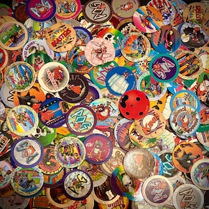 Może przedstawiać: Duża kolekcja okrągłych tekturowych dysków do gry, znanych jako pogs, zawierająca różnorodne kolorowe ilustracje graficzne, postacie z kreskówek i logotypy. Zestaw obejmuje rozmaite wzory, motywy i jasne kolory rozrzucone razem.