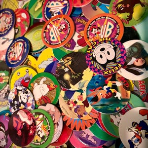 May include: A vibrant assortment of vintage pogs, circular cardboard discs, showcasing cartoon characters such as Mickey Mouse, Felix the Cat, and Animaniacs. The pogs display diverse designs, logos, and text, including "Kids' WB" and "Walt Disney".