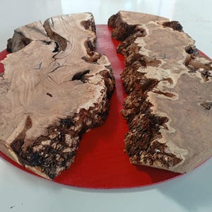 May include: Two pieces of wood with a natural wood grain pattern, joined together with a red epoxy resin. The wood has a rough, textured surface and is a light brown color. The epoxy resin is a bright red color and fills the gap between the two pieces of wood.