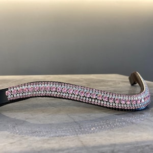 Puede incluir: Un frontal de caballo de cuero negro con una fila de diamantes de imitación rosas y transparentes.