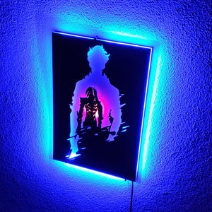 Puede incluir: Una pieza de arte mural negra con la silueta de una persona y una figura en su interior, enmarcada por una luz LED azul. La figura interior se destaca con tonos rosas y morados, creando un contraste llamativo.