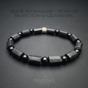 Könnte beinhalten: Schwarzes Turmalin-Armband mit dem Text "BLACK TOURMALINE = STONE OF PROTECTION & GROUNDING". Das Armband besteht aus schwarzen, geometrisch geformten Perlen und runden Perlen, mit einer silberfarbenen Perle in der Mitte.