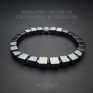 May include: A dark grey hematite bracelet featuring square beads and a silver accent bead. The bracelet is presented on a dark grey backdrop. Text at the top reads "HEMATITE - STONE OF GROUNDING & STRENGTH". The brand name "INSIGNIS" is at the bottom.