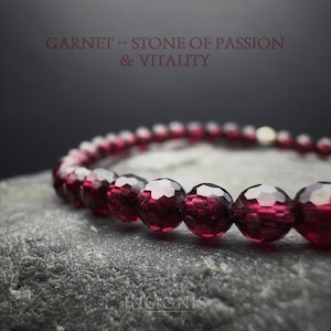 Könnte beinhalten: Ein Armband aus facettierten, tiefroten Granatperlen. Das Armband wird auf einer grauen, strukturierten Oberfläche präsentiert. Der Text oben lautet "GARNET - STONE OF PASSION & VITALITY". Der Markenname "INSIGNIS" steht unten.