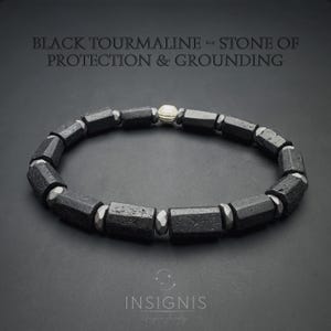 Könnte beinhalten: Ein Perlenarmband mit zylindrischen schwarzen Turmalinsteinen, die sich mit kleinen Metallperlen und einer einzelnen silberfarbenen, strukturierten Perle abwechseln. Der Text BLACK TOURMALINE - STONE OF PROTECTION & GROUNDING und INSIGNIS ist sichtbar.