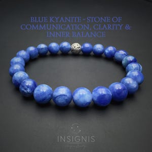 Könnte beinhalten: Ein Armband aus runden, polierten blauen Kyanit-Perlen, die in einem Kreis angeordnet sind, mit einer einzelnen verzierten silberfarbenen Metallperle. Der Text oben lautet BLUE KYANITE - STONE OF COMMUNICATION, CLARITY & INNER BALANCE, unten INSIGNIS.