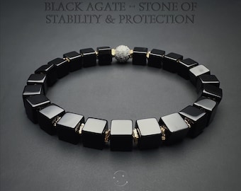 May include: Black agate bracelet featuring square beads and a silver-colored accent bead. The bracelet is strung together with gold-colored connectors. Text at the top reads "BLACK AGATE - STONE OF STABILITY & PROTECTION". The brand name "INSIGNIS" is at the bottom.