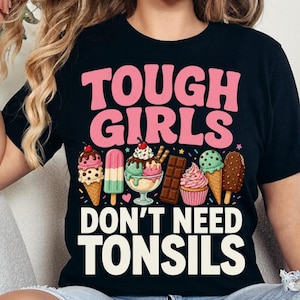 May include: A black t-shirt featuring the pink text TOUGH GIRLS and white text DON'T NEED TONSILS. Between the text is a colourful graphic of various desserts including ice cream cones, a popsicle, a chocolate bar, and a cupcake with sprinkles.