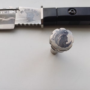 May include: A silver knife with a black handle and a silver cap with the words "Zenith Knives" and a wolf head design engraved on it.