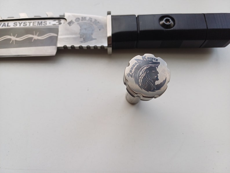 May include: A silver knife with a black handle and a silver cap with the words "Zenith Knives" and a wolf head design engraved on it.