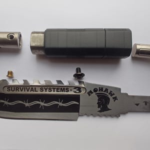 May include: A disassembled survival knife with a black handle, a silver blade with a barbed wire design, and the text "SURVIVAL SYSTEMS - 3" and "MOHAWK" printed on the blade.