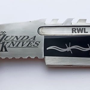 May include: A silver and black knife with a black handle and a serrated blade. The blade has a barbed wire design and the text "RWL - 34" and "ZUNDA KNIVES" is engraved on the blade.
