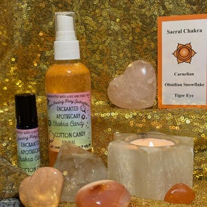 Puede incluir: Un surtido de artículos espirituales, que incluyen un frasco rociador, un frasco con rodillo, cristales y un candelabro con una vela encendida. El frasco rociador está etiquetado como "Enchanted Apothecary Chakra Candy Cotton Candy". Una tarjeta enumera "Sacral Chakra" y piedras.