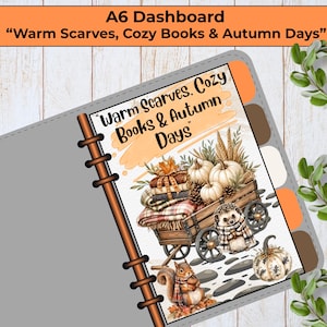 Puede incluir: Una página de agenda A6 con el texto "Warm Scarves, Cozy Books & Autumn Days" y una ilustración de un carro de madera lleno de calabazas, libros y una manta a cuadros, junto a un erizo y una ardilla con una bufanda.