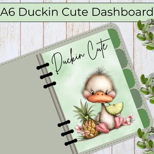 May include: An A6 planner dashboard featuring a light green background with a cartoon duckling holding a lime slice, a pineapple, and pink flowers. The text Duckin Cute is printed in black script above the duckling, with black binder rings.