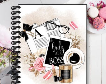 May include: Spiral-bound notebook with a decorative design featuring a tablet with the text "be lady be BOSS", a cup of coffee, a candle, lipstick, and macarons. The design includes flowers, glasses, and a black bow.