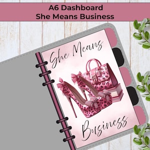 May include: An A6 dashboard planner insert featuring the text She Means Business. The design includes a pair of pink leopard print high-heeled shoes with bows and a matching pink leopard print handbag resting on a stack of books on a light background.
