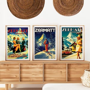 May include: Three vintage travel posters for Zermatt, Switzerland. The posters feature a skier on a mountain, a group of women in front of a mountain, and a woman in a white dress standing in front of a mountain with a car in the foreground. The posters are framed in wood and are displayed on a wooden shelf.