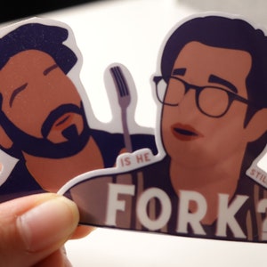 May include: Two illustrated cartoon characters, one with a beard and one with glasses, are holding a fork. The text "Is he still holding the fork?" is written below the characters.