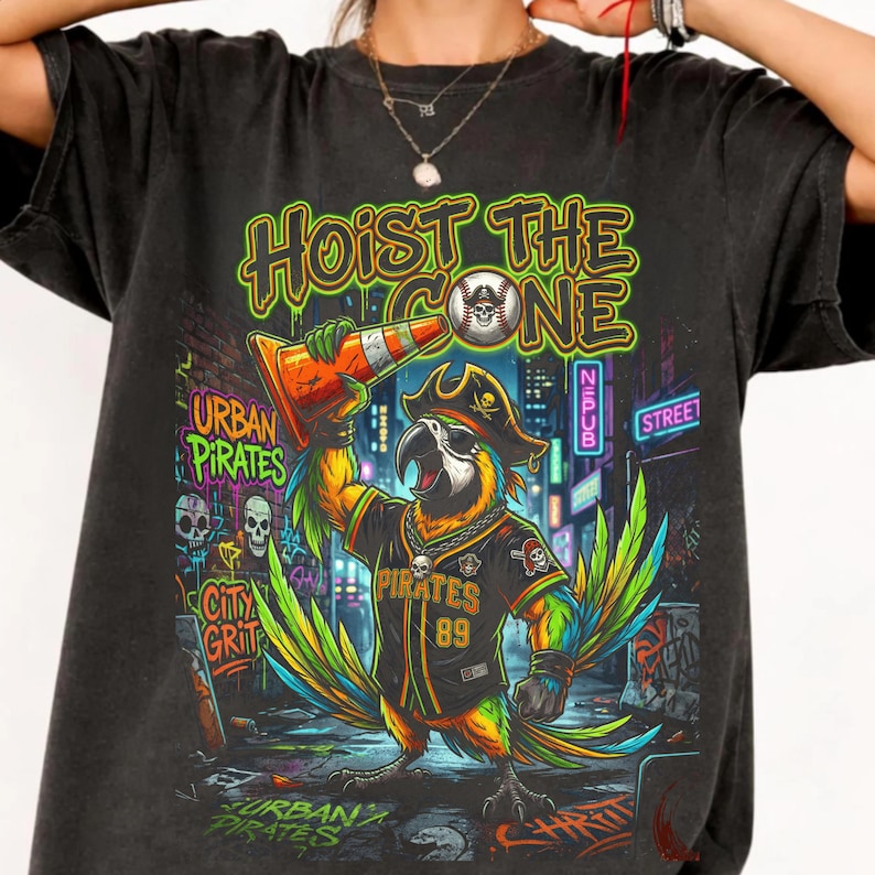 K&ouml;nnte beinhalten: Schwarzes T-Shirt mit einem bunten Papagei, der einen Piratenhut und ein Baseball-Trikot tr&auml;gt und einen orangefarbenen Verkehrskegel h&auml;lt. Der Text lautet "Hoist the Cone". Das Design beinhaltet Totenk&ouml;pfe und die Worte "Urban Pirates."